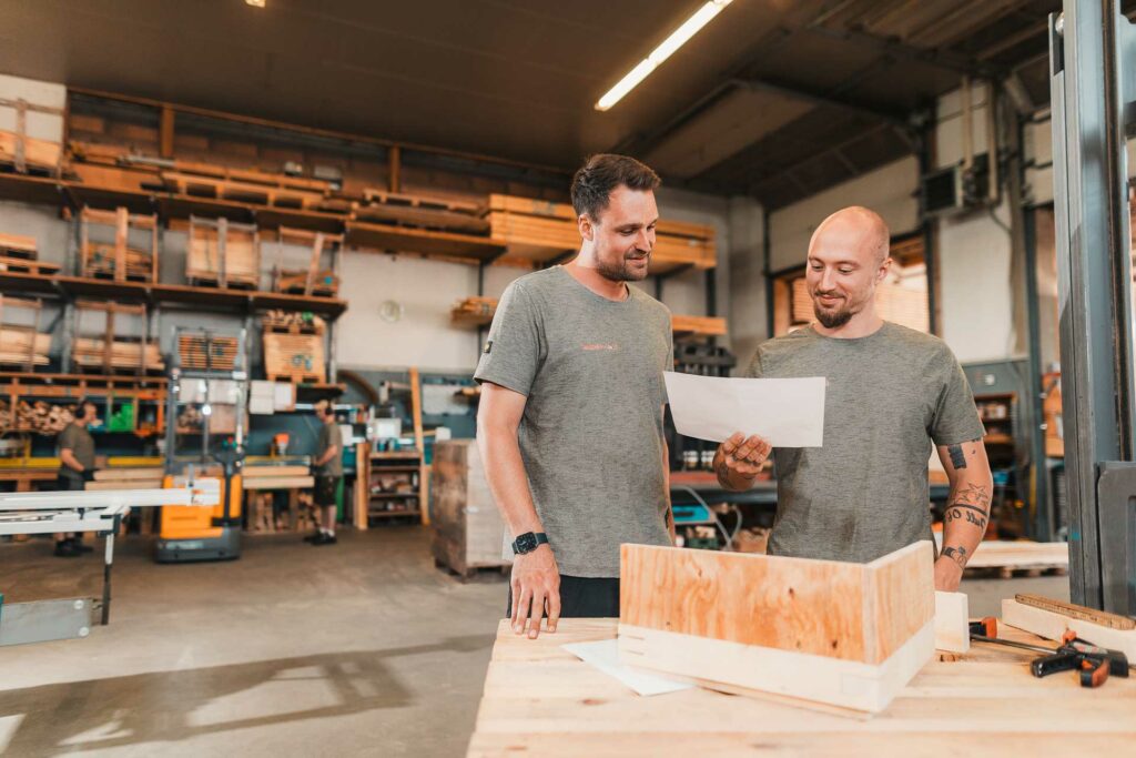 Exportverpackung-Sonderverpackung-Wecker Zwei Mitarbeiter in der Konstruktonsplanung einer Transportkistenzeichnung aus Holz